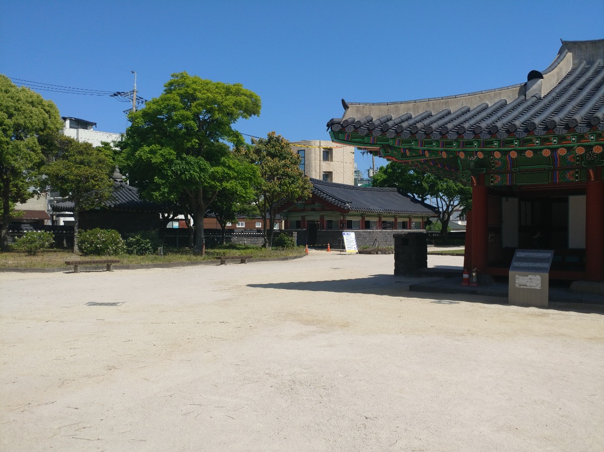 제주목관아 통로 사진입니다. 기와집과 흙으로 된 길 그리고 등받이가 없는 벤치 2개가 있습니다.