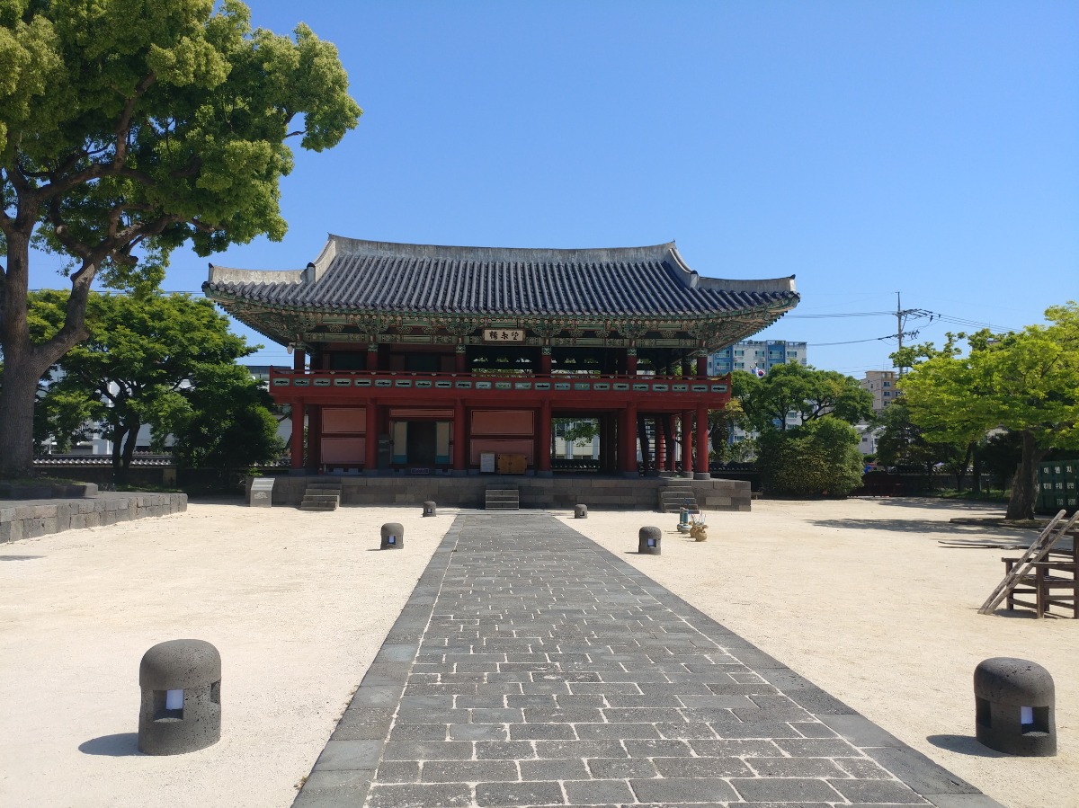 제주목관아 기와집을 정면에서 본 모습입니다. 돌로 된 평평한 길과 그 끝에 돌로 된 계단이 있습니다. 기와집은 총 2층으로 2층으로 올라가는 계단이 있습니다.