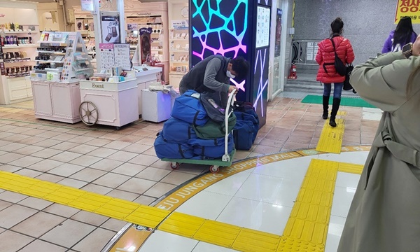 만남의 광장 내 손수레에 짐을 싫고 가는 사람이 보이는 사진입니다.