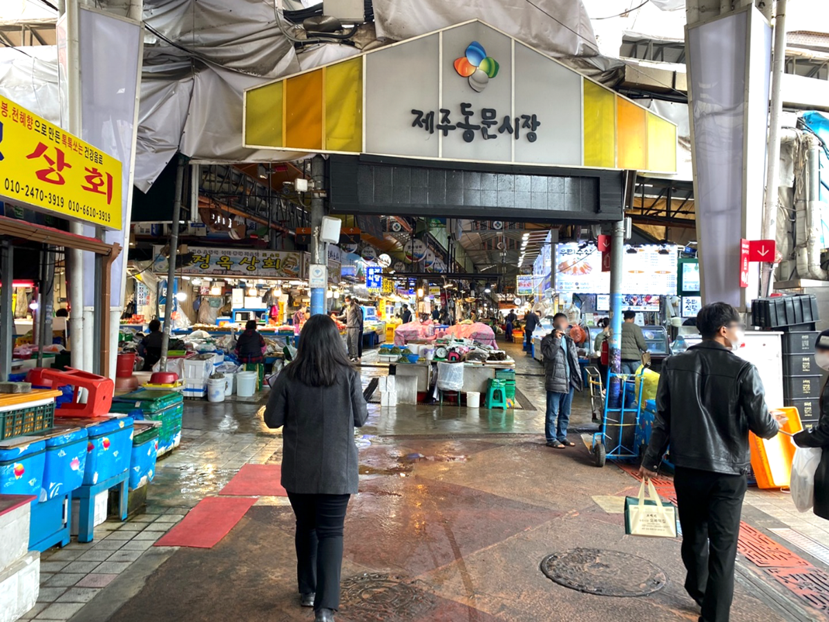 동문시장 내부 사진입니다. 제주동문시장이라고 적힌 글귀가 천장에 있습니다. 앞에는 해산물들을 파는 가계들이 보입니다.
